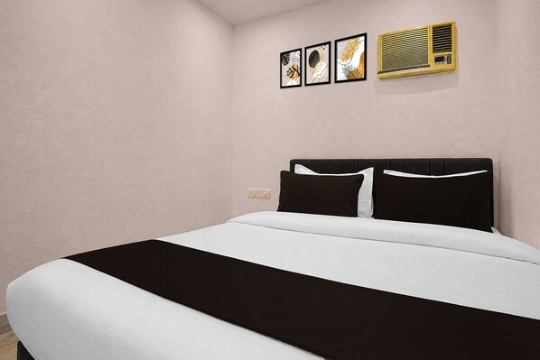 Una habitación de hotel con una cama, aire acondicionado de pared y tres obras de arte enmarcadas.