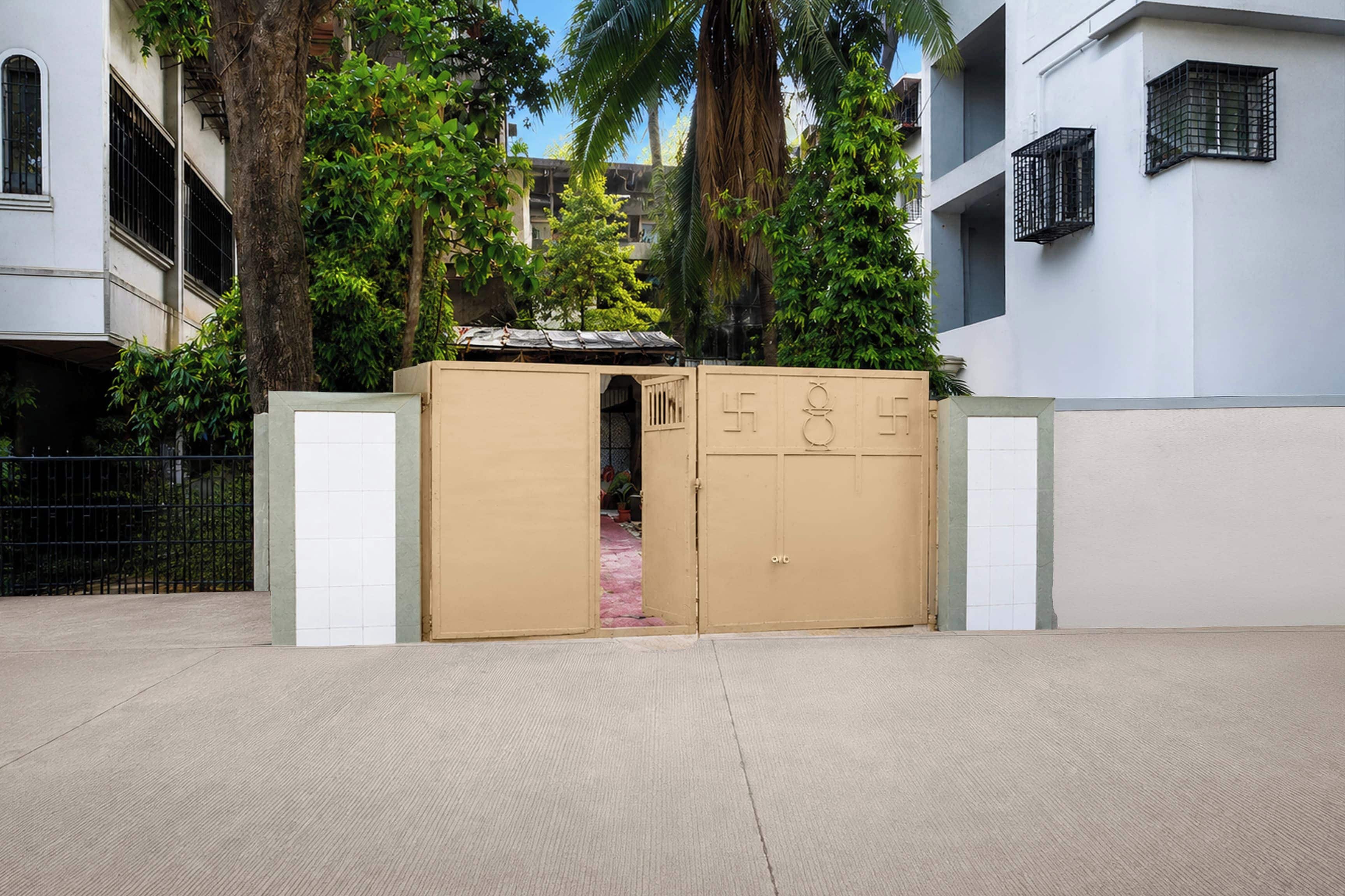 Una entrada protegida con una reja metálica y una puerta, rodeada de árboles y edificios.