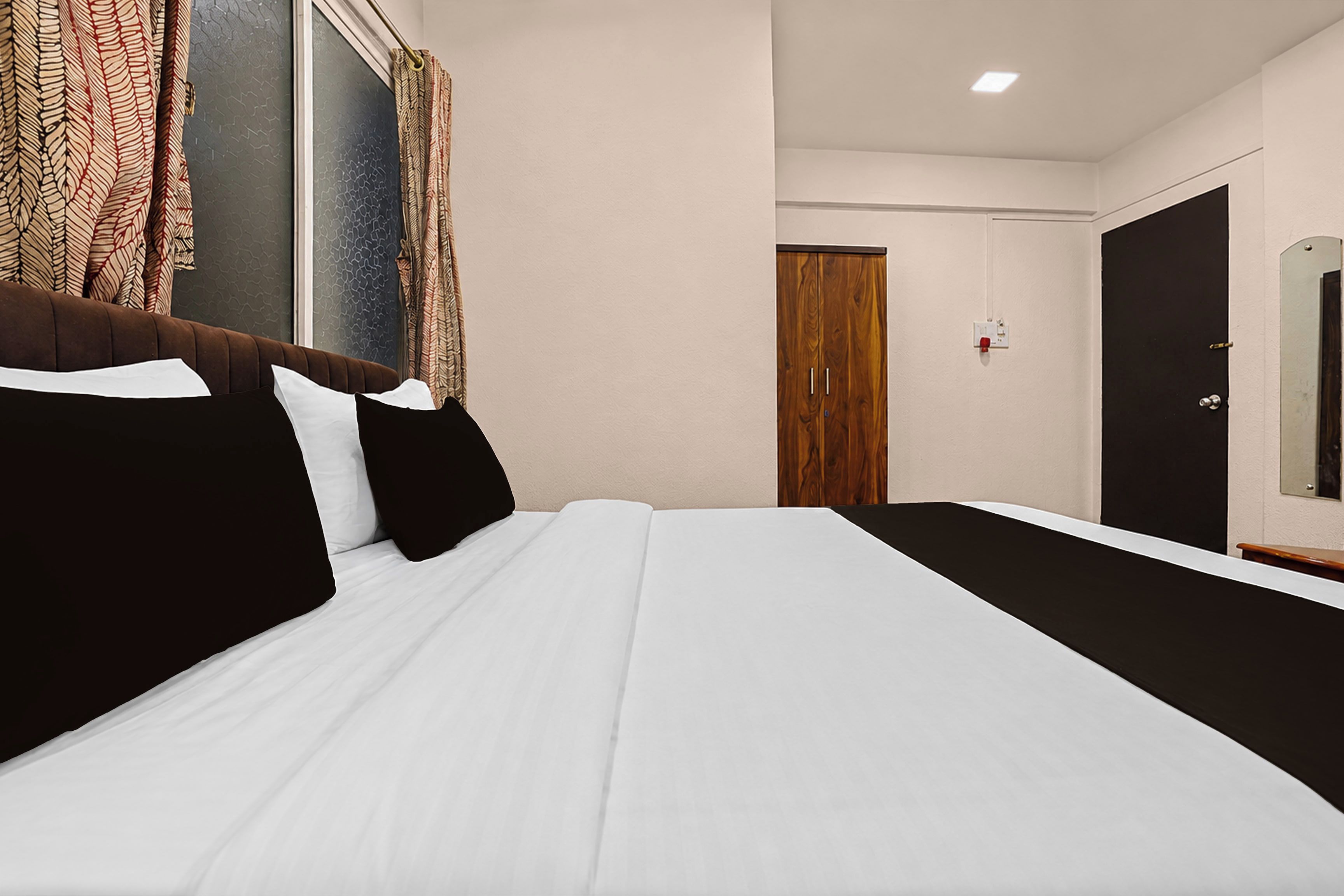 Habitació d'hotel amb llit, armari de fusta, porta i finestra amb cortines.