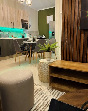 A modern kitchen with wooden cabinets, a dining area with a round table and chairs, and a living space with a sofa and a coffee table. - Cozy Retreat in Carlswald 264 (Johannesburg)