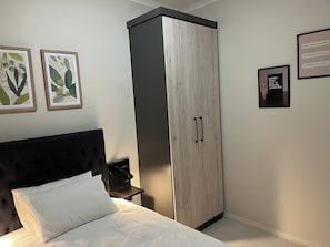 A bedroom with a bed, a wardrobe, and two framed artworks on the wall. - Cozy Retreat in Carlswald 264 (Johannesburg)
