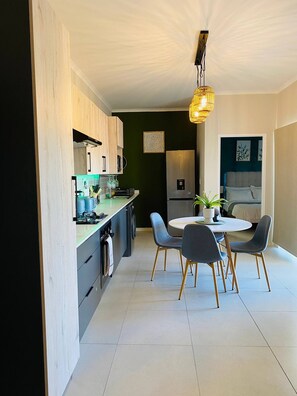 A modern kitchen with a dining area, featuring a central island, built-in appliances, and a hanging light fixture. - Cozy Retreat in Carlswald 264 (Johannesburg)