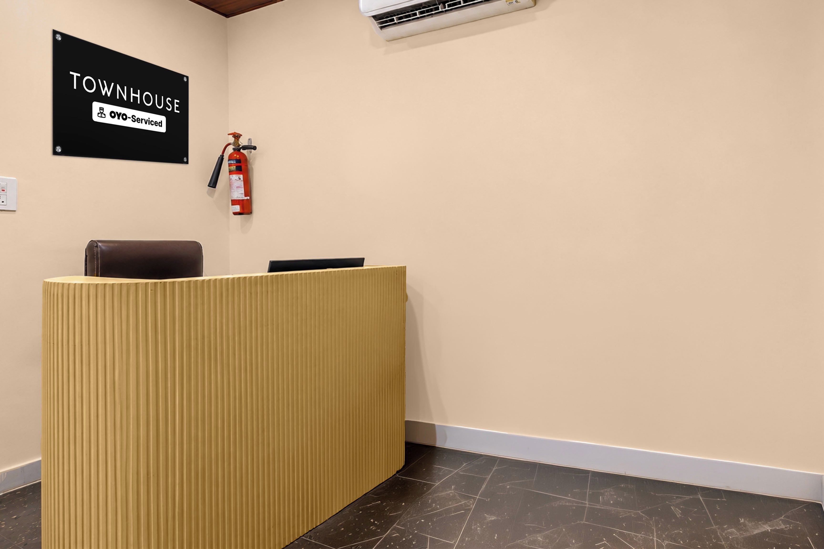 Uma mesa de recepção com uma placa em cima, um extintor de incêndio fixado na parede e um aparelho de ar condicionado sobre a mesa.
