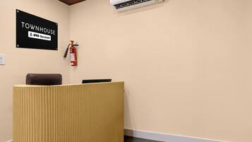 Uma mesa de recepção com uma placa em cima, um extintor de incêndio fixado na parede e um aparelho de ar condicionado sobre a mesa.