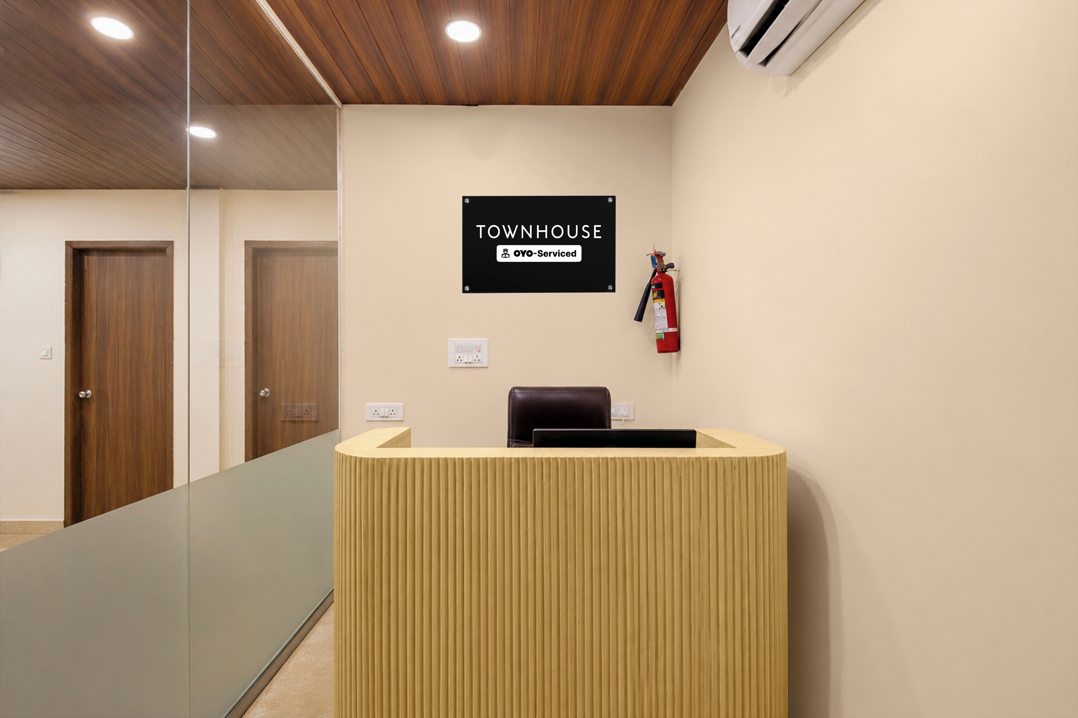 A reception area with a wooden reception desk, a sign indicating it's serviced by Oyo, and a fire extinguisher on the wall.