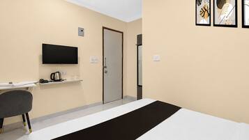 A hotel room with a bed, a desk, a chair, a television, and a door.
