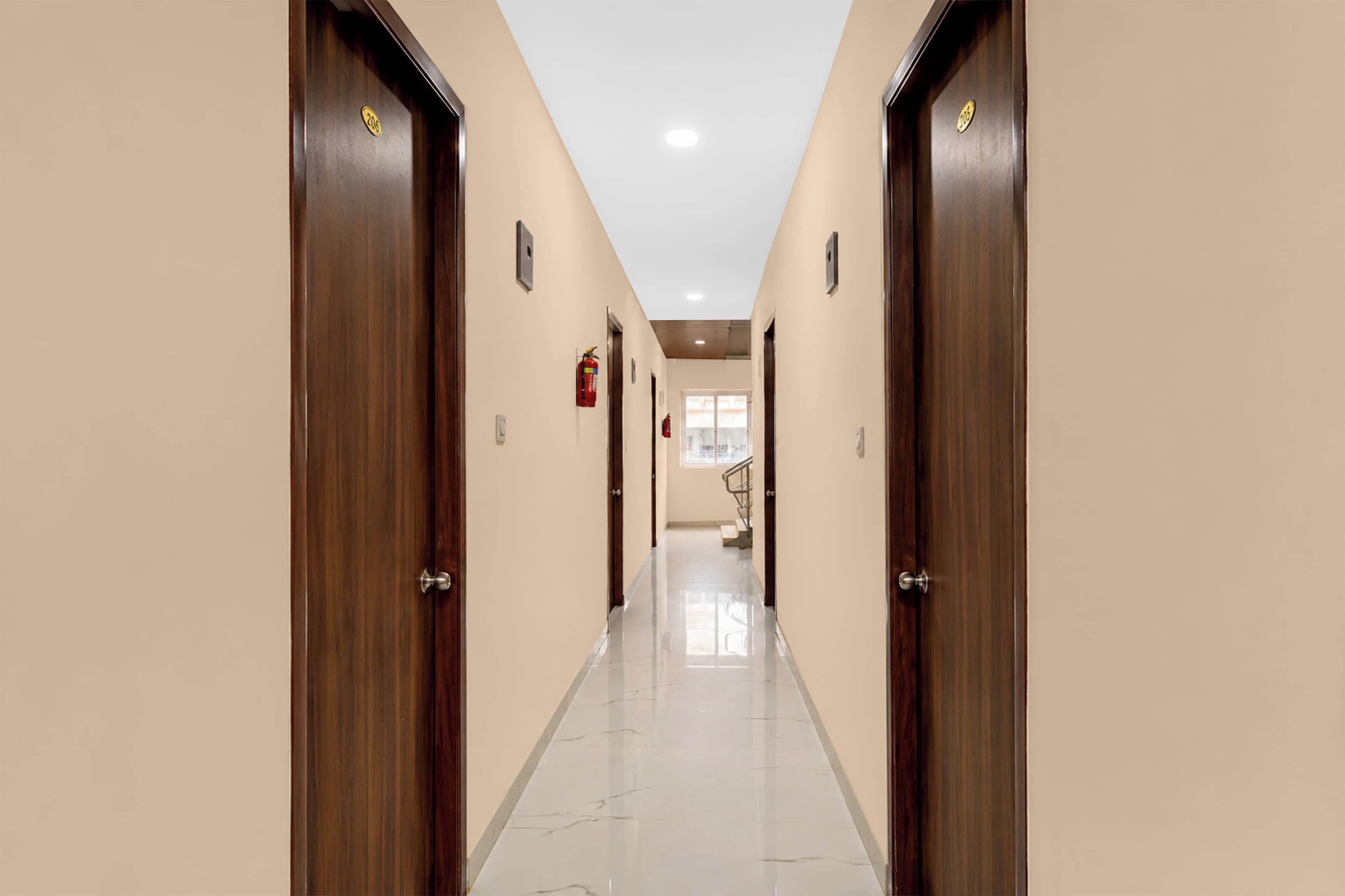 A hotel hallway with wooden doors, a tiled floor, and a fire extinguisher on the wall.
