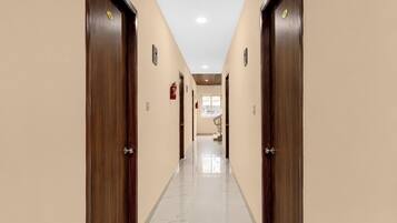 A hotel hallway with wooden doors, a tiled floor, and a fire extinguisher on the wall.