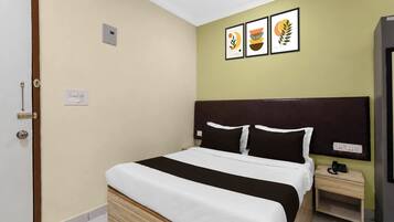 Una habitación de hotel con cama, mesita de noche y toma de corriente en la pared.