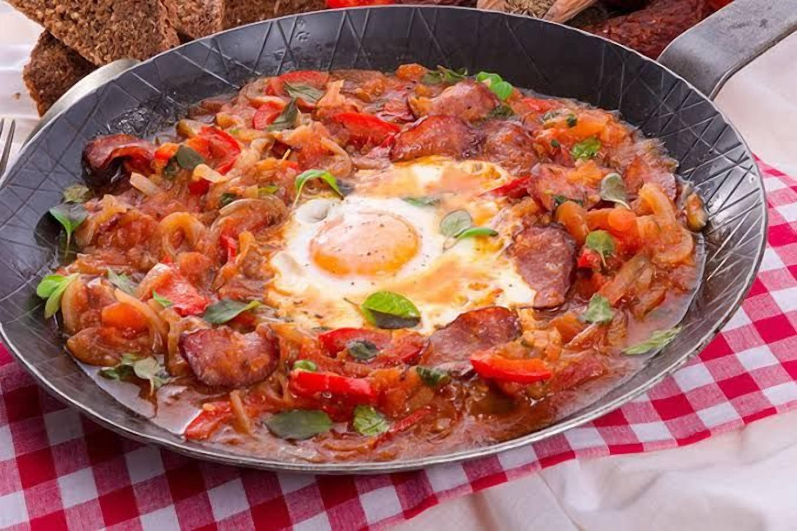 Un plato de desayuno con huevos, salchicha y verduras en una sartén.