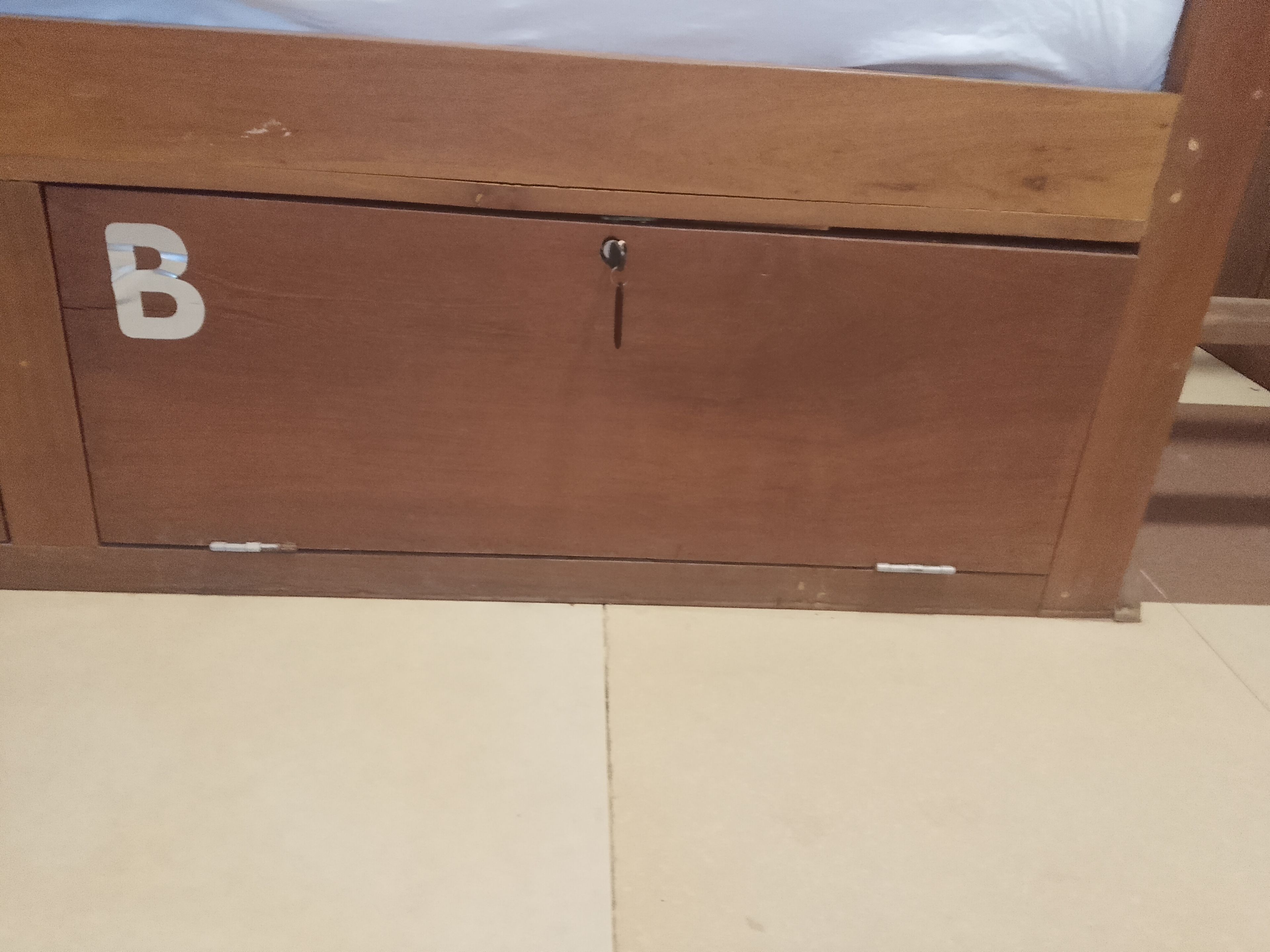 A wooden cabinet with a lock, a visible letter 'B' on the side, and a tiled floor.