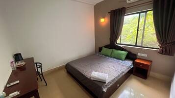 A bedroom with a bed, a bedside table, a desk, a chair, an air conditioning unit, and a window with curtains.