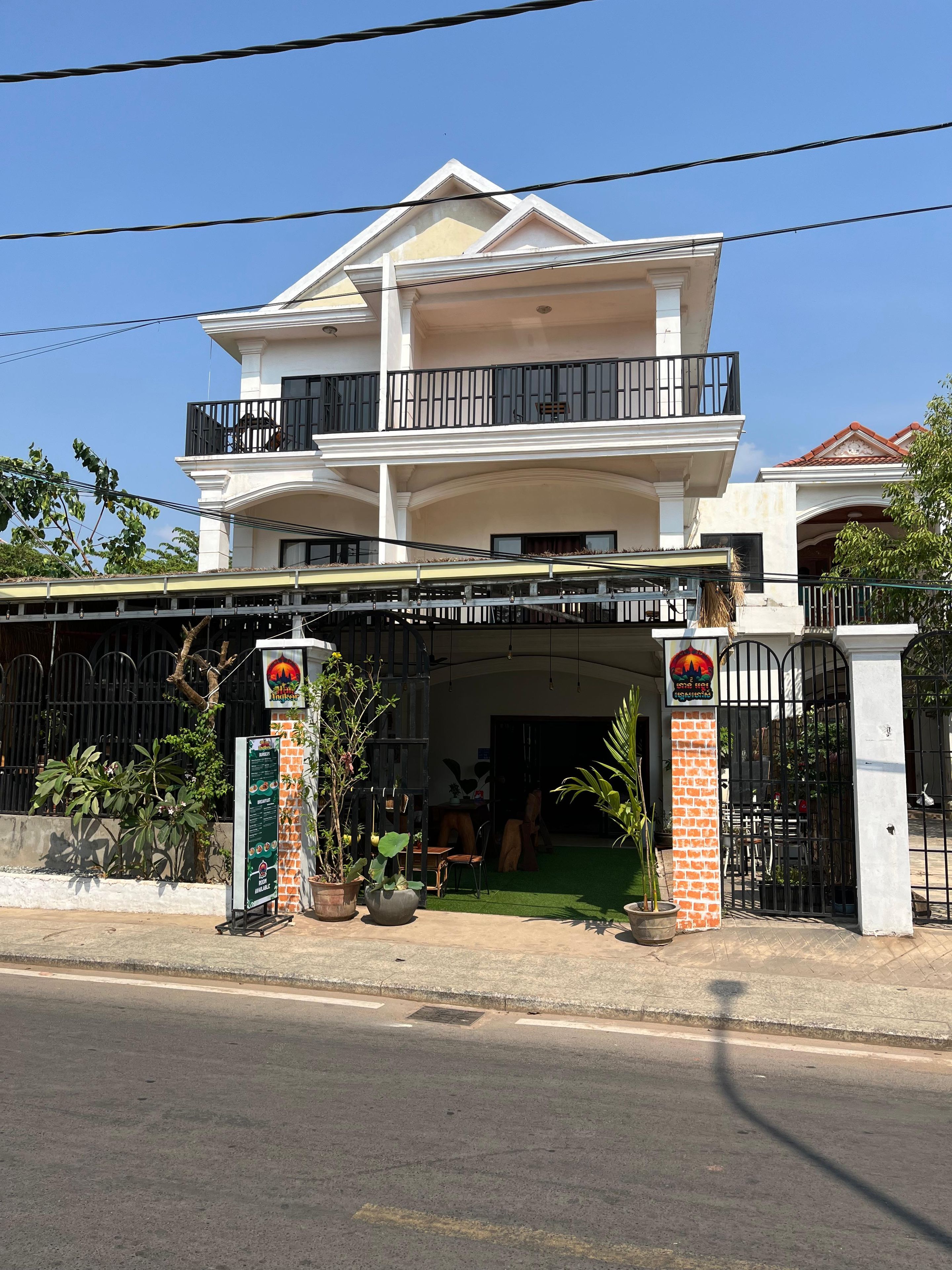 Un edificio de dos pisos con un balcón, entrada protegida por una reja y un letrero.