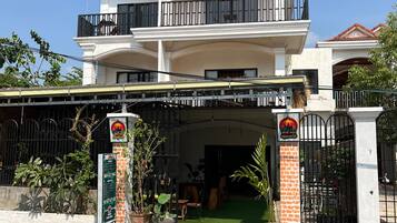 Un edificio de dos pisos con un balcón, entrada protegida por una reja y un letrero.