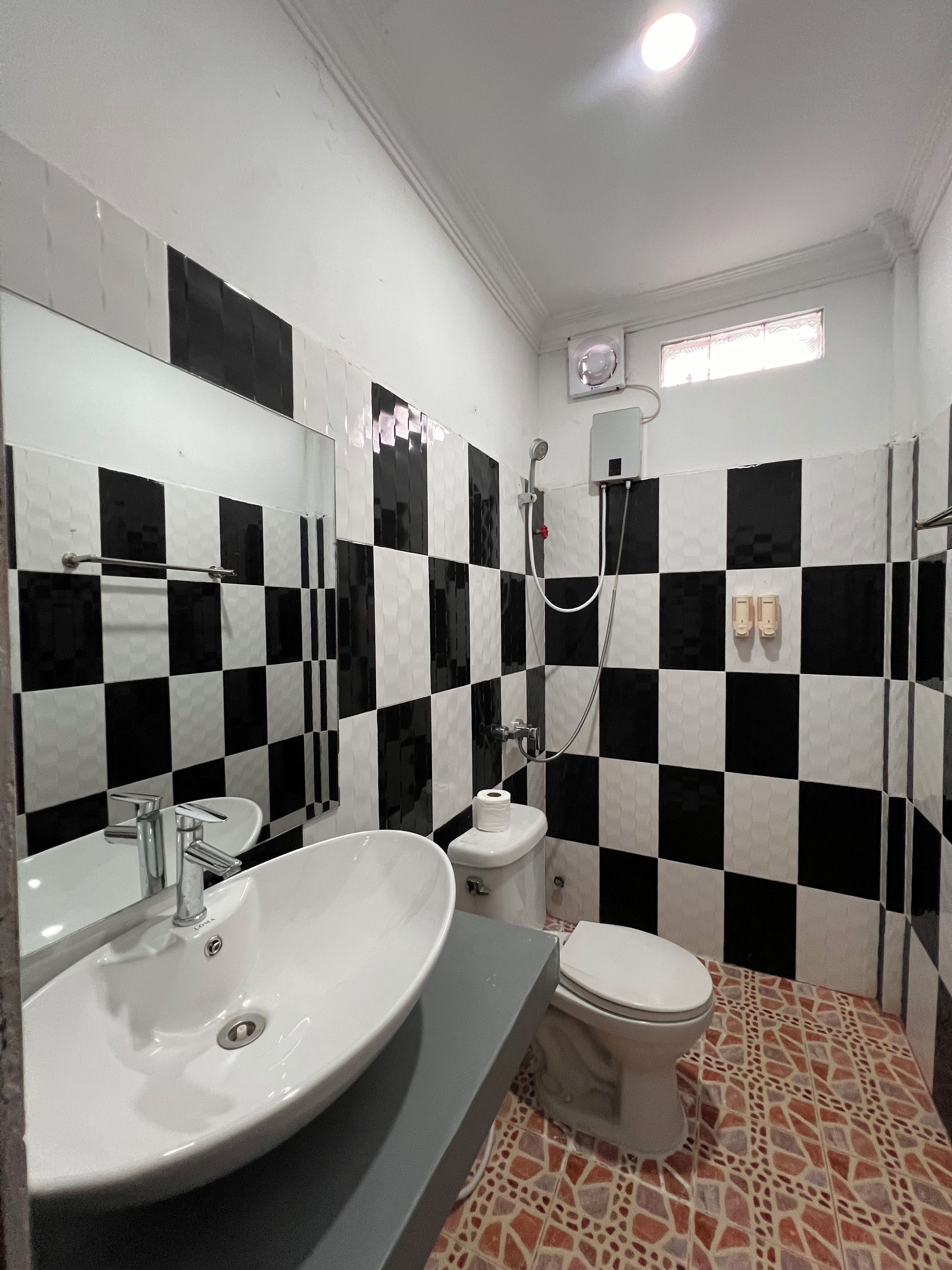 A bathroom with a checkered black and white tile wall, a white sink, a toilet, and a shower area.