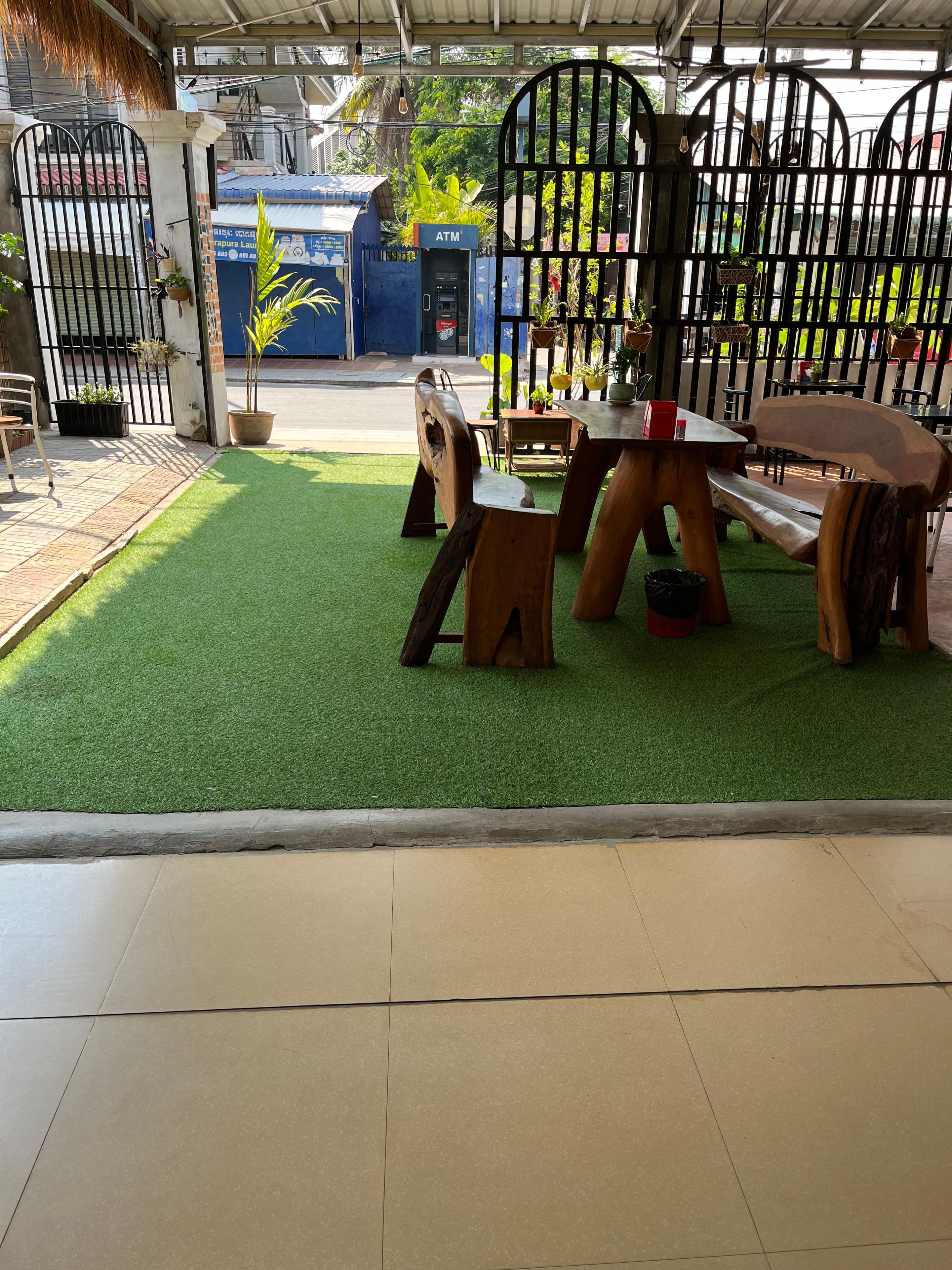 Un área con mesas y sillas al aire libre, un cajero automático pequeño y una entrada con reja.