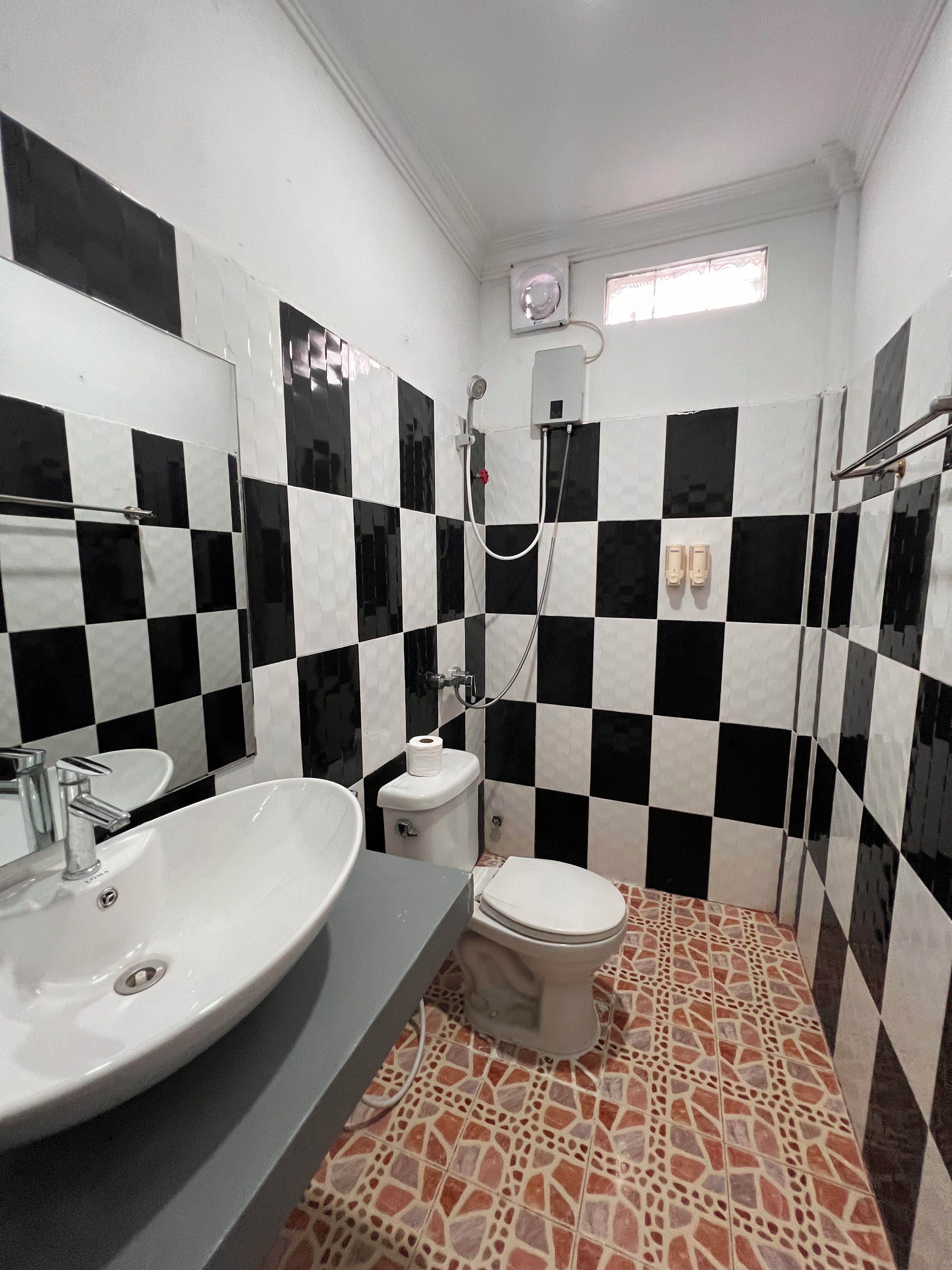 A bathroom with a checkered black and white tile wall, a white sink, a toilet, and a shower area.