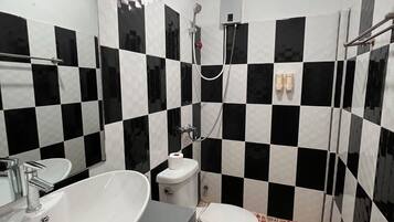 A bathroom with a checkered black and white tile wall, a white sink, a toilet, and a shower area.