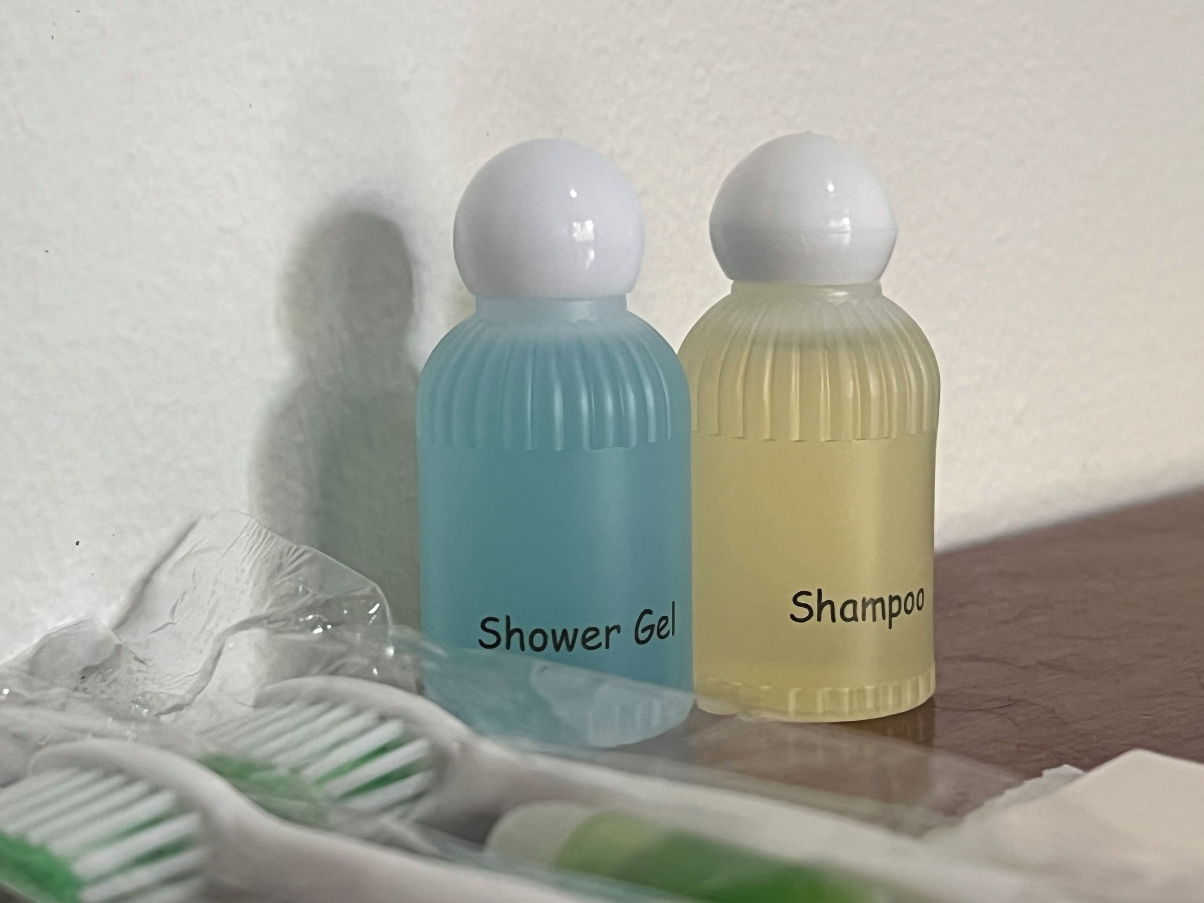 Dos botellas de artículos de aseo, una con la etiqueta 'Gel de ducha' y otra 'Champú', sobre una encimera de baño.