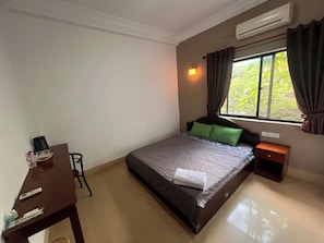 Un dormitorio con cama, mesita de noche, escritorio, silla y ventana con cortinas.