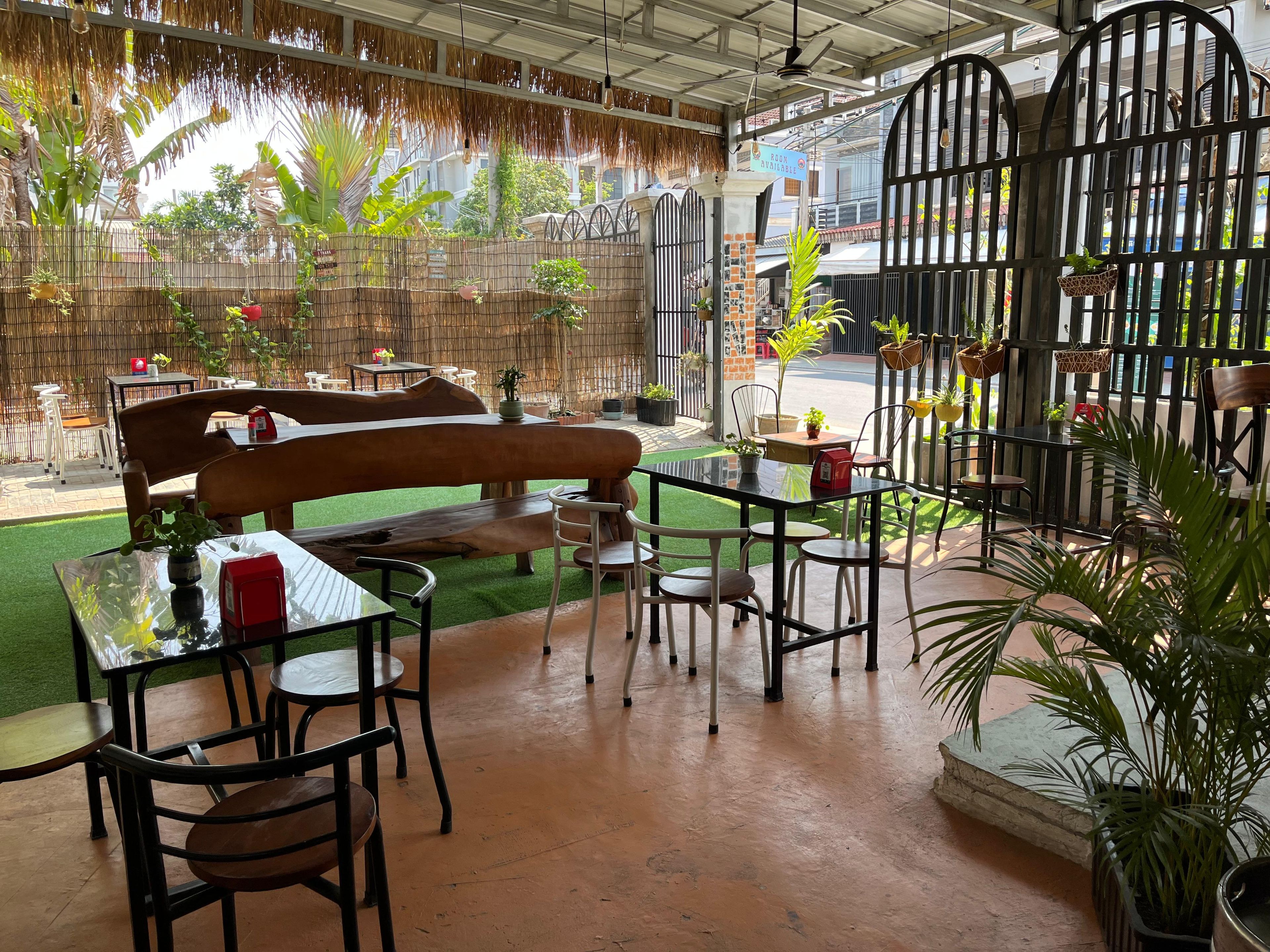 An outdoor seating area with tables, chairs, and a bench, surrounded by potted plants and a bamboo fence.