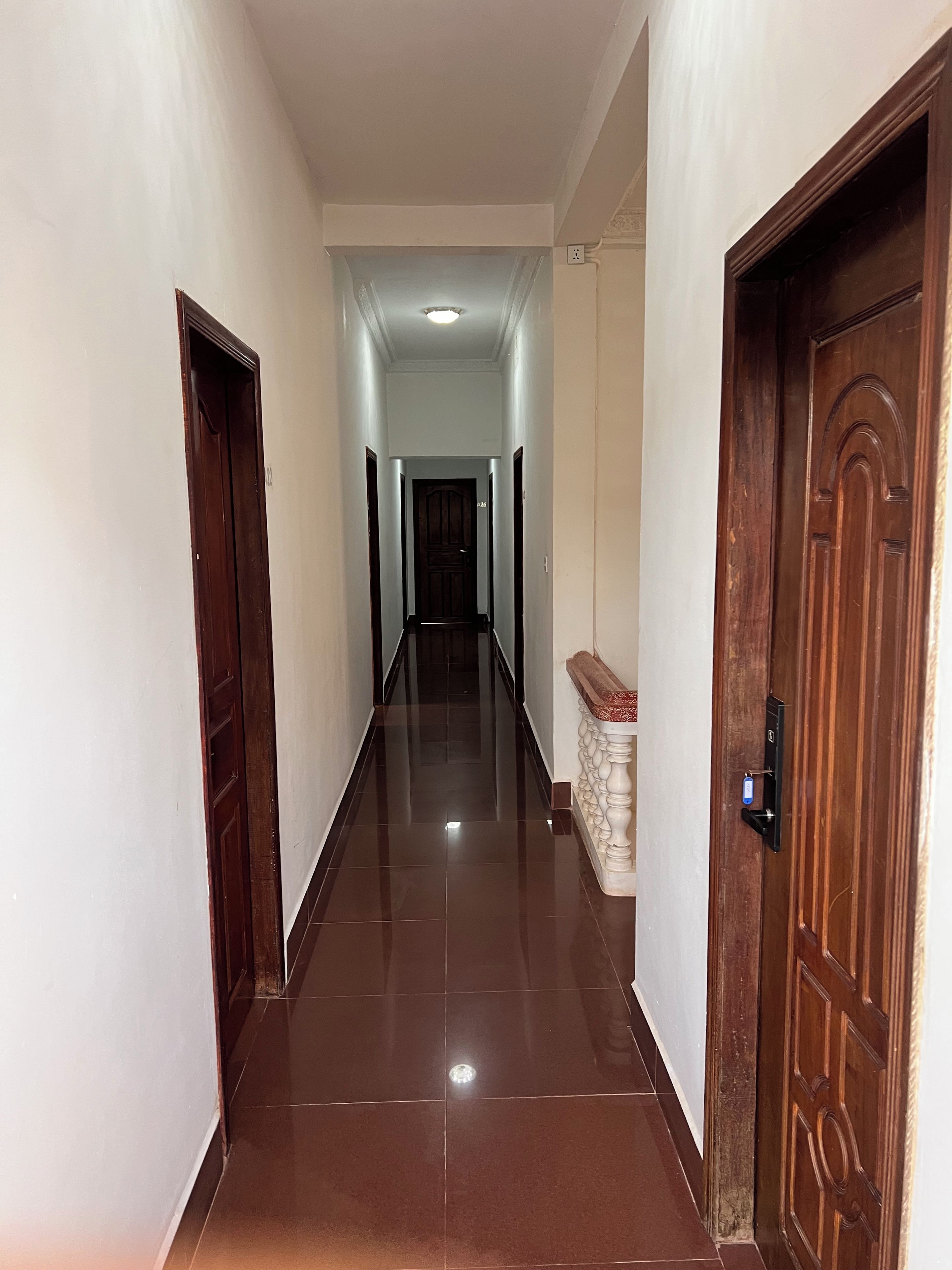 Un pasillo con piso de baldosas brillantes, puertas de madera y una lámpara en el techo.