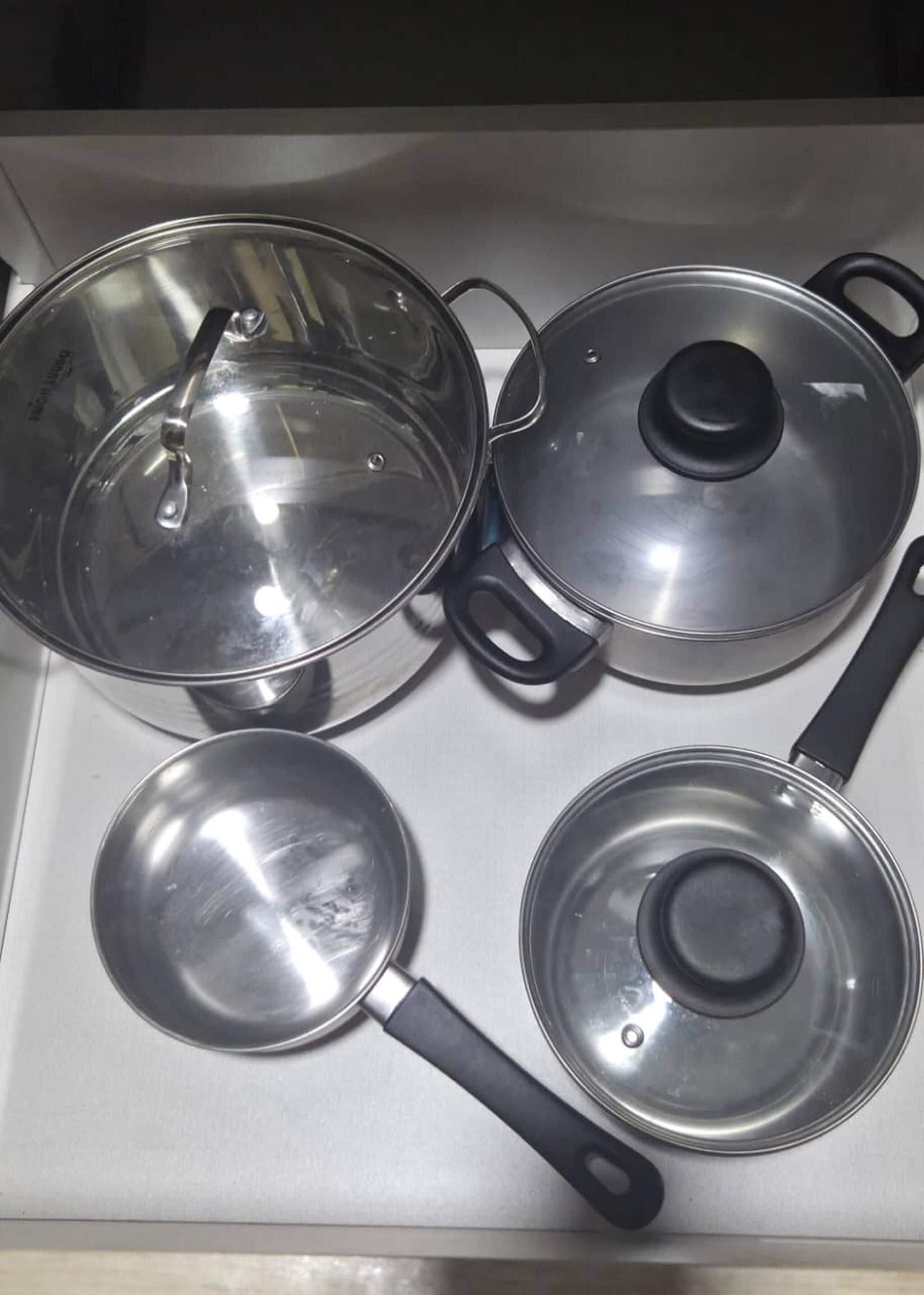 Une cuisine avec quatre casseroles et poêles en acier inoxydable posées sur un plan de travail.