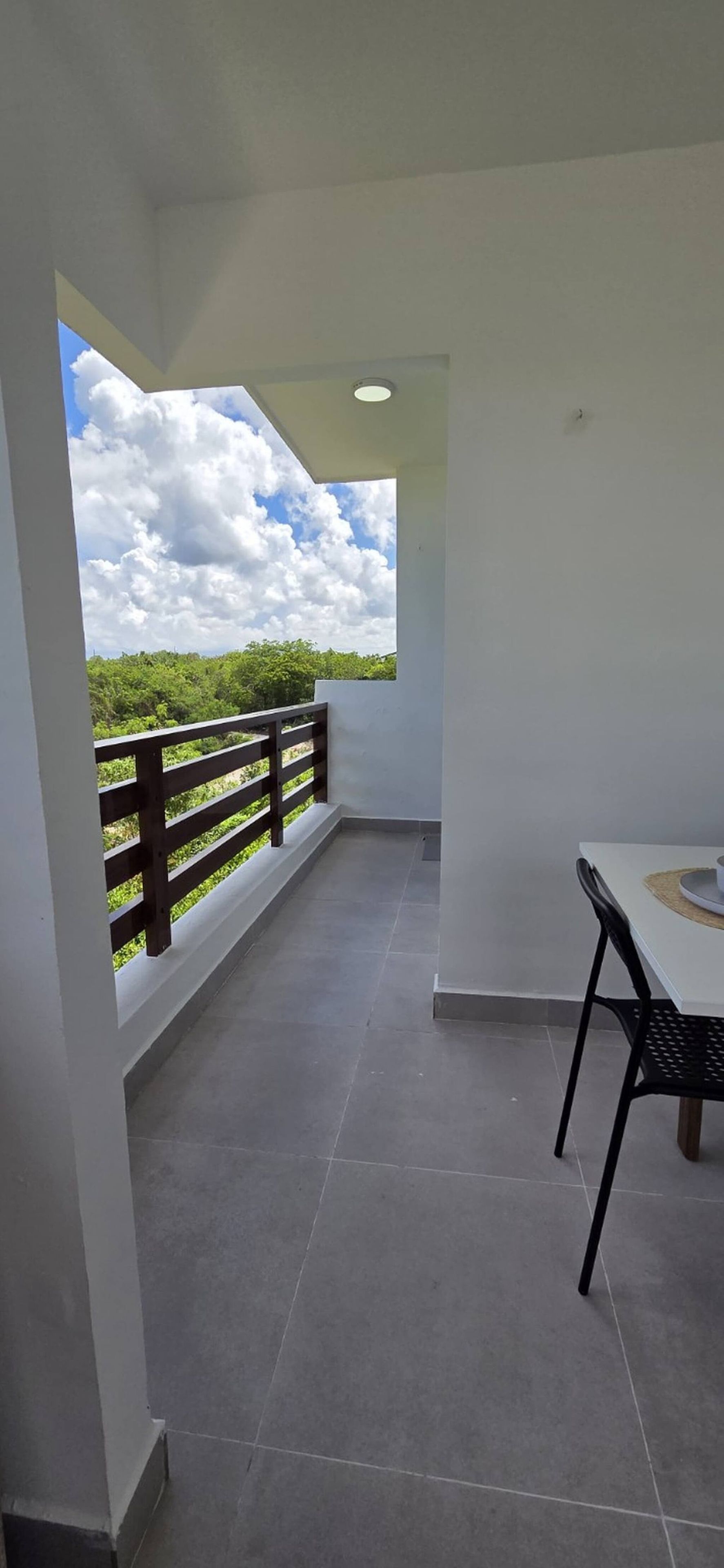 A balcony with a view of greenery and clouds, a table with chairs, and a ceiling light.
