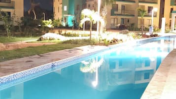 Una piscina con superficie de agua azul cristalina, rodeada por un jardín bien cuidado con palmeras y arbustos.