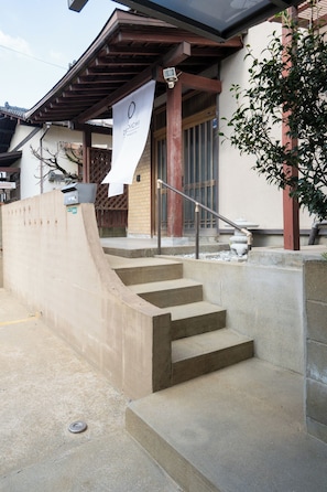 A set of concrete steps leading to a building entrance with a metal handrail.