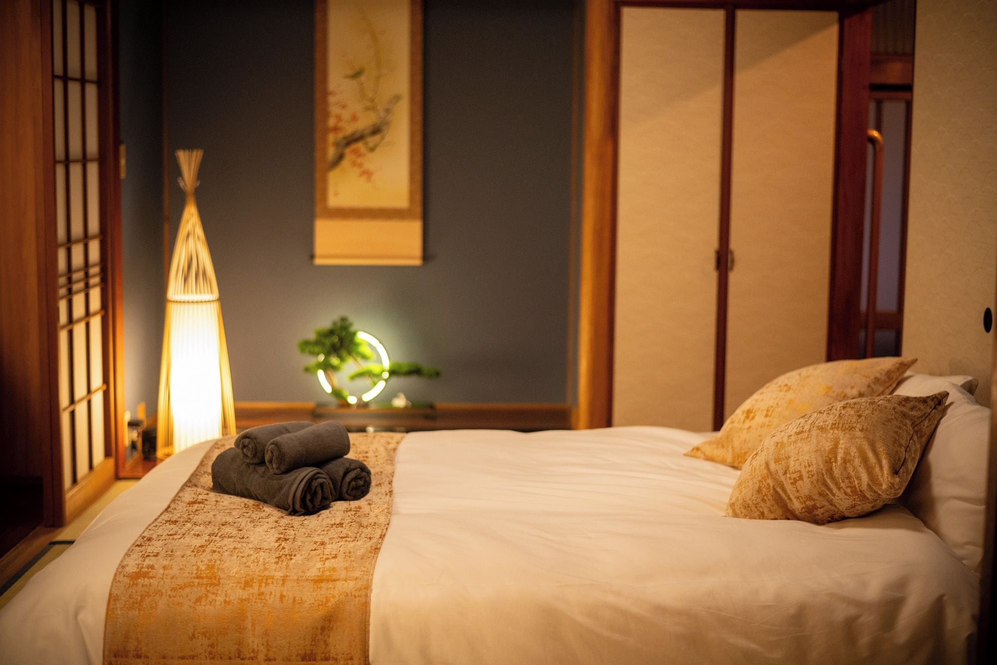 A neatly made bed with a blanket and pillows, a bedside lamp, and a wall-mounted painting.