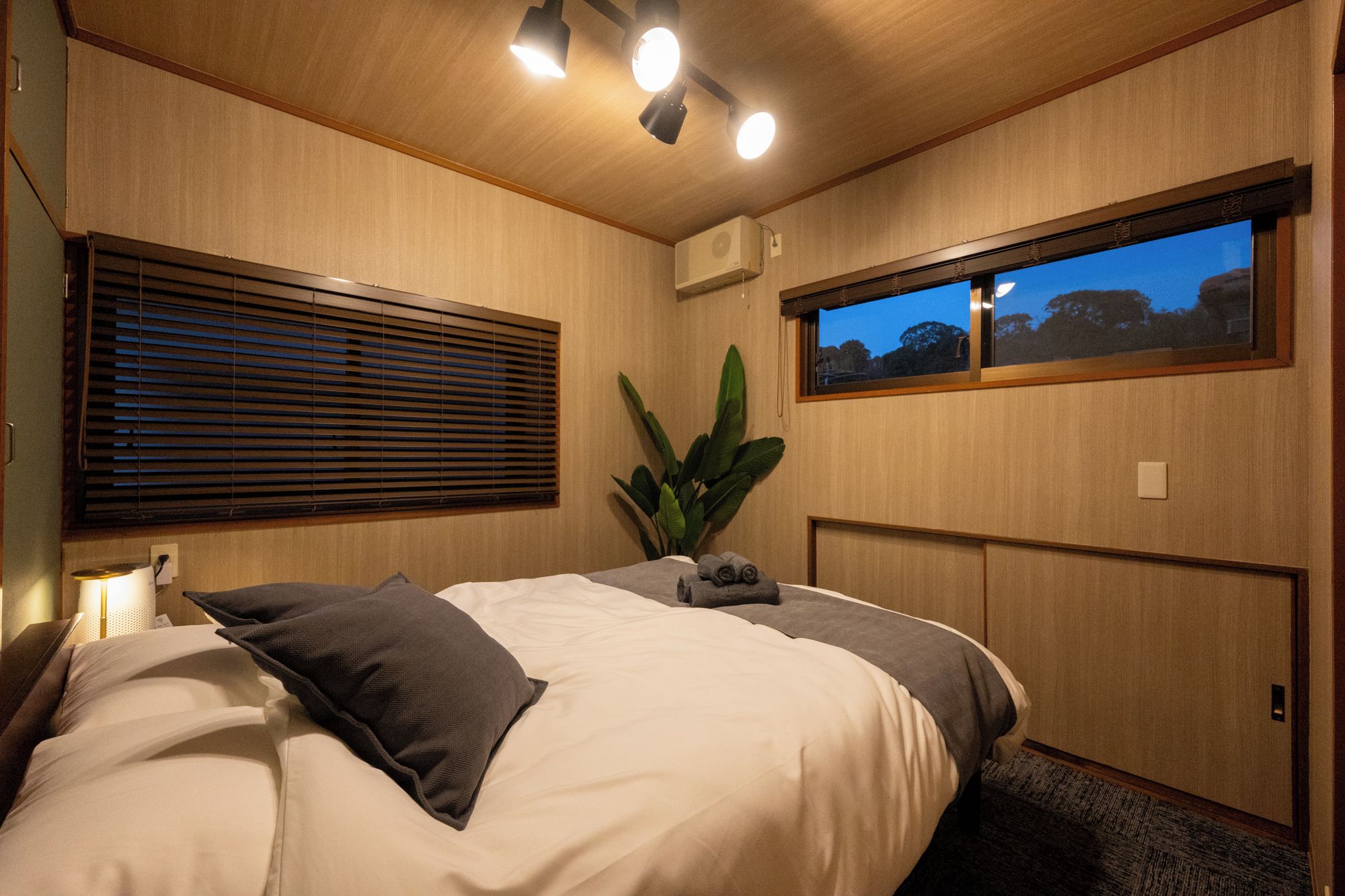 Une chambre à coucher avec un lit, une fenêtre donnant sur un beau paysage, une plante et un luminaire au plafond.