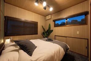 A bedroom with a bed, a window with a view, a plant, and a ceiling light fixture. - Zeroichi Hotel House Hakata (Fukuoka)