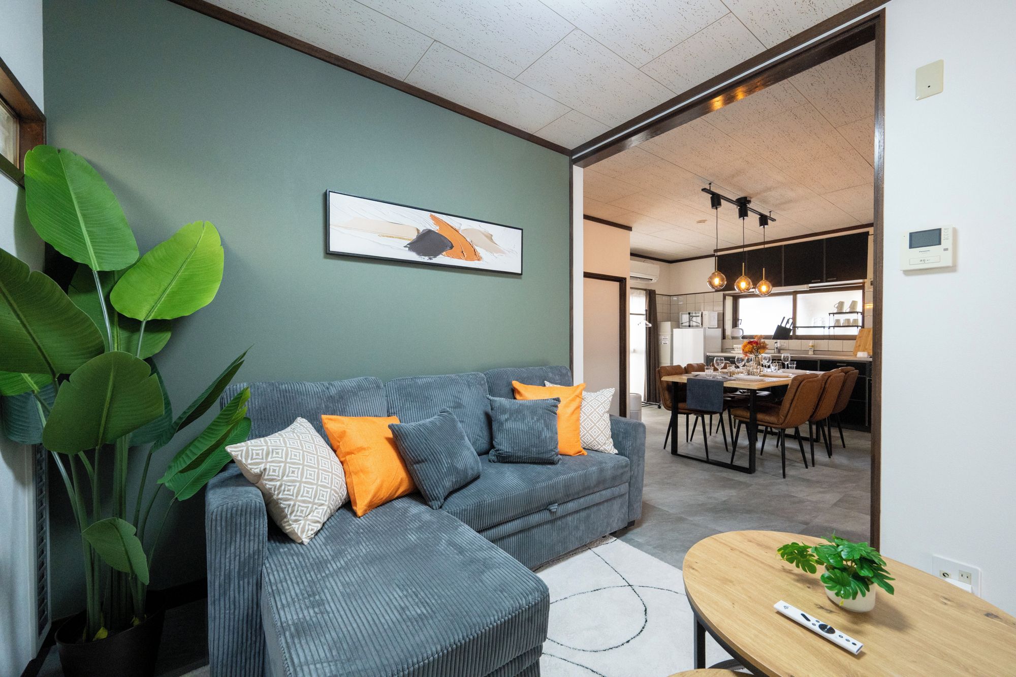 A modern living room with a grey sofa, a dining area, and a kitchen in the background.