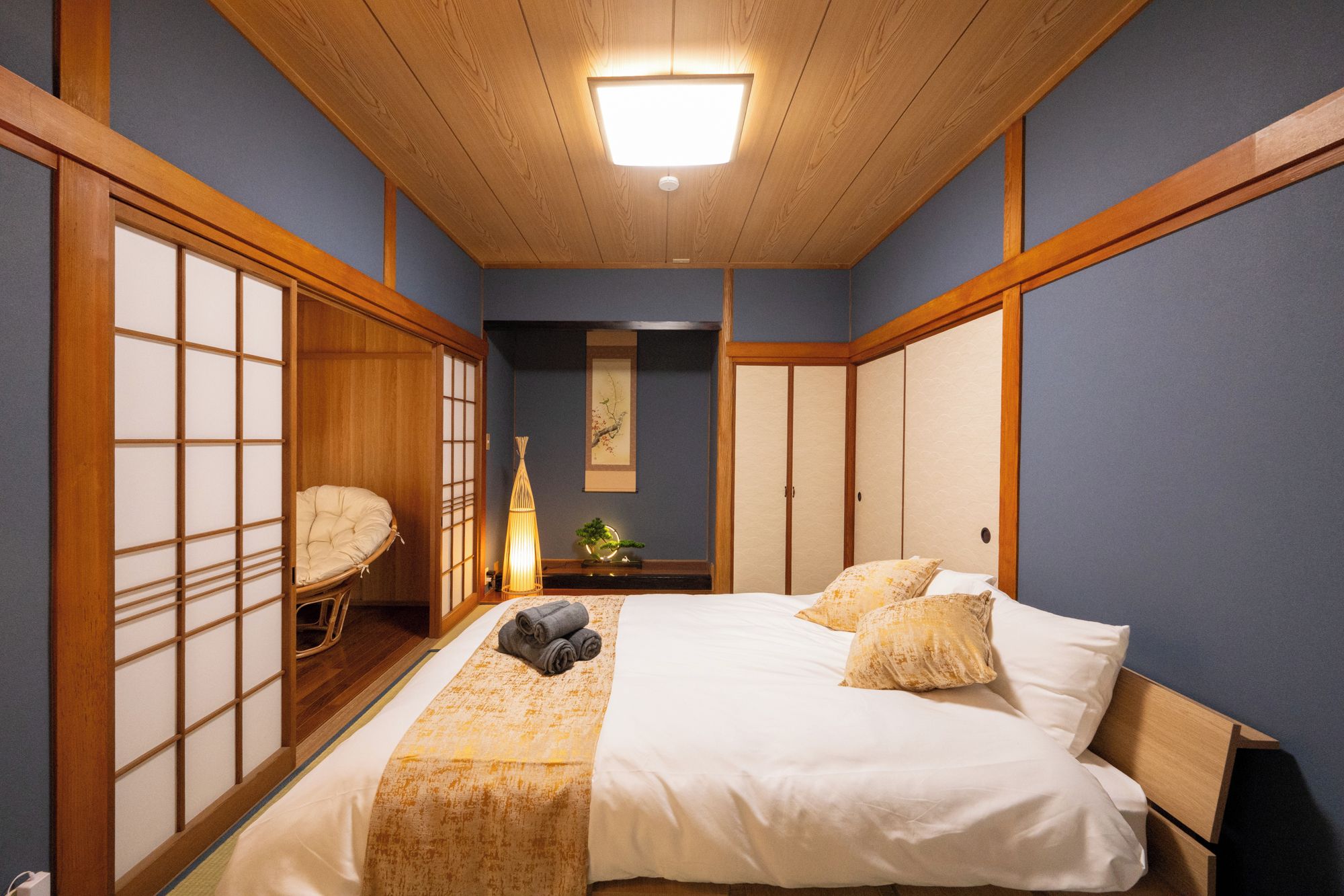 A traditional Japanese-style bedroom with a bed, futon, sliding doors, and a hanging lamp.