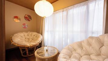 A room with a large window, a hanging light fixture, and two round wicker chairs.