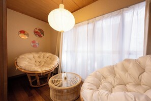 A room with a large window, a hanging light fixture, and two round wicker chairs.