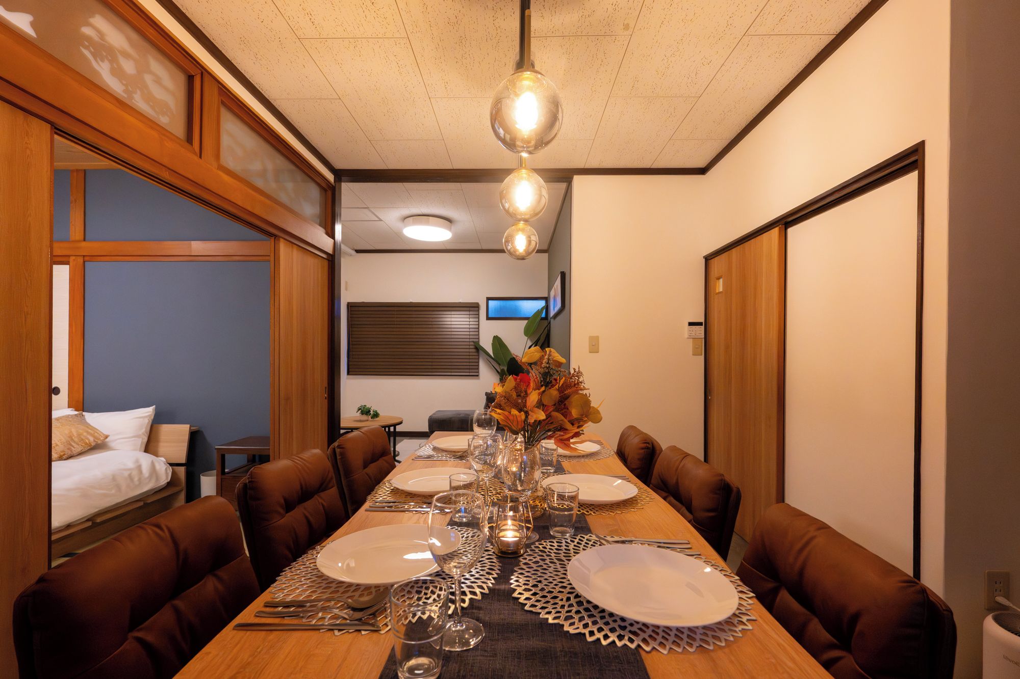Un coin repas avec une longue table en bois dressée pour le repas, entourée de chaises marron à revêtement.