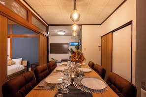 A dining area with a long wooden table set for a meal, surrounded by brown upholstered chairs. - Zeroichi Hotel House Hakata (Fukuoka)