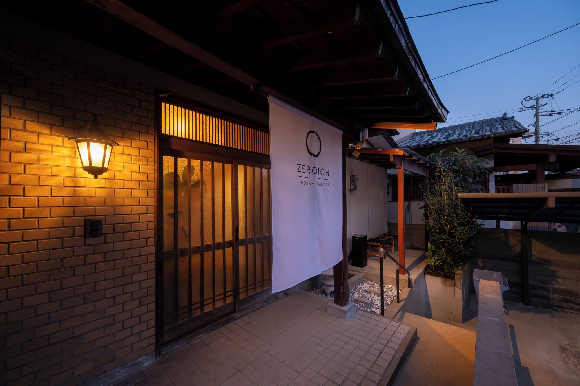 Un bâtiment à la façade en briques, avec une porte d’entrée en bois et une enseigne indiquant « ZEROICHI HOUSE HAKATA ».