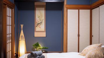 A bedroom with a bed, a wall-mounted painting, a traditional Japanese-style lamp, and a sliding door.