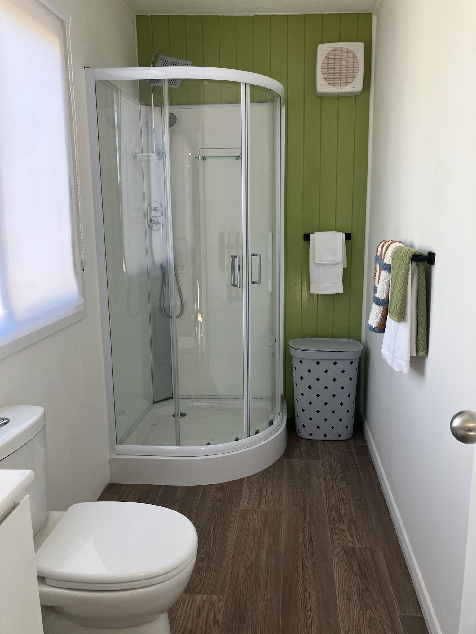 A bathroom with a glass-enclosed shower, a toilet, a trash bin, and a towel rack with towels.