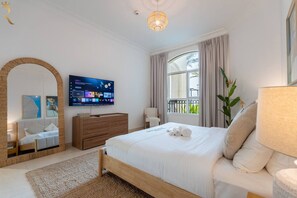 A hotel room with a bed, a TV, a large mirror, a window with curtains, and a plant. - 2BR | Balcony | Yas Island | Pool & Gym (Abu Dhabi)