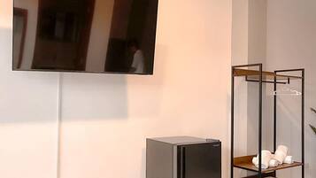 Una habitación moderna con un televisor de pantalla plana montado en la pared, un refrigerador empotrado y un estante de madera con toallas.