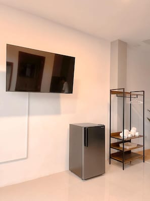 A modern room with a flat-screen TV mounted on the wall, a built-in refrigerator, and a wooden shelf unit with towels. - The Island Palms Homestay (Alaminos City)