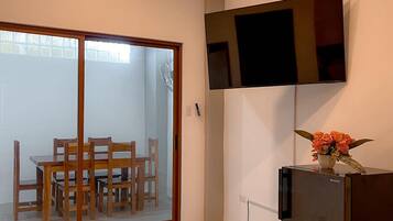 Een moderne keuken met een koelkast, een flatscreen televisie aan de muur en een eethoek met houten stoelen en een glazen deur naar een terras.