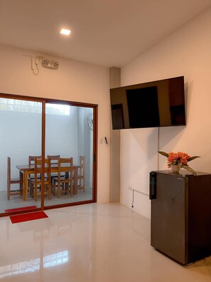 A modern kitchen with a refrigerator, a flat-screen TV mounted on the wall, and a dining area with wooden chairs and a glass door leading to a patio. - The Island Palms Homestay (Alaminos City)