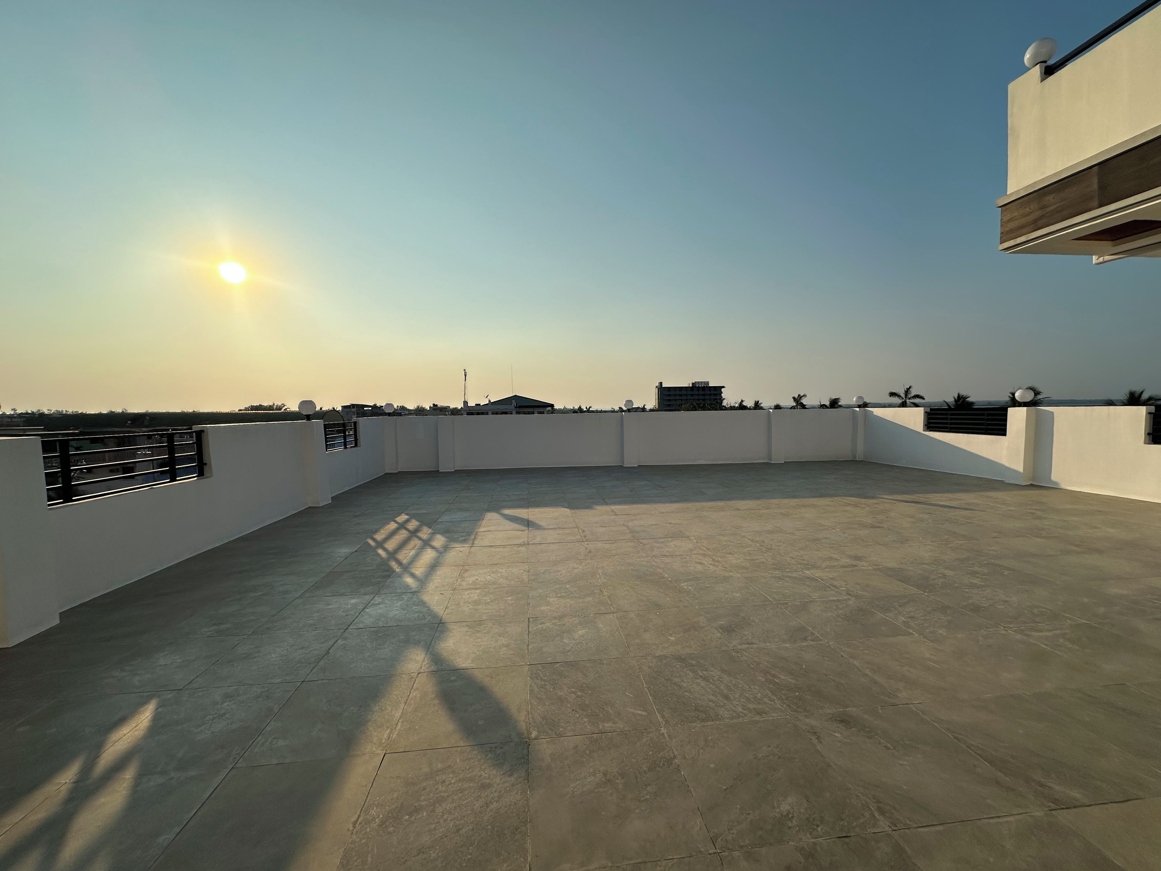 Una terraza en la azotea con cielo despejado, el sol proyectando sombras y edificios a lo lejos.