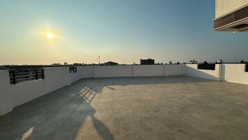 Una terraza en la azotea con cielo despejado, el sol proyectando sombras y edificios a lo lejos.