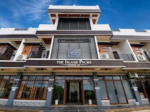 A modern hotel with a prominent logo, large windows, and air conditioning units. - The Island Palms Homestay (Alaminos)